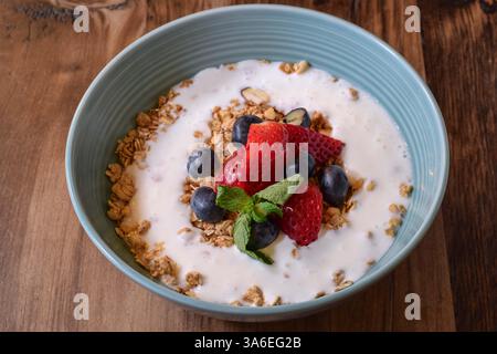 Ciotola blu di muesli da colazione con yogurt, fragole fresche e mirtilli su un tavolo rustico in legno Foto Stock