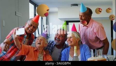 Amici anziani che indossano cappelli da festa scattano selfie durante le feste di compleanno a casa. amicizia, riunione, divertimento, gioioso, senior, felicità Foto Stock
