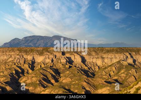 Una stupenda catena montuosa incombe sui canyon profondamente erosi sotto un vasto cielo azzurro con nuvole mostruose Foto Stock