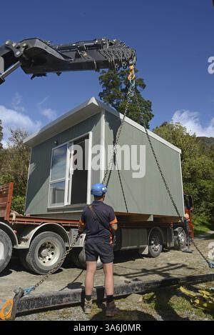 GREYMOUTH, NUOVA ZELANDA, 21 OTTOBRE 2020: Un operatore di gru lavora per sollevare un piccolo edificio da un camion sui suoi pali Foto Stock