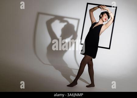 Modella in posa creativa con cornice per immagini, proietta ombre spettacolari sulla parete, copia spazio Foto Stock