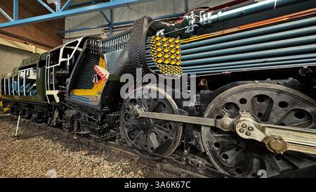 Locomotiva a vapore tagliata che rivela componenti interni, compresi tubi e meccanismi di caldaia, esposti su binari ferroviari in un edificio industriale Foto Stock