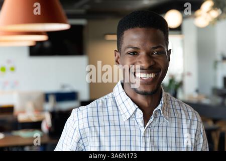 Uomo sorridente in ufficio che indossa una camicia a scacchi, sicuro di sé e felice Foto Stock