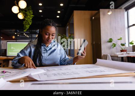 Donna professionista che esamina i progetti architettonici e utilizza un tablet in un ufficio moderno Foto Stock