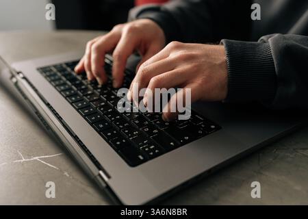 Primo piano ritagliato di una digitazione maschile non riconoscibile del programmatore sulla tastiera di un notebook, immerso nello sviluppo software o nella codifica, seduto a un tavolo vicino Foto Stock