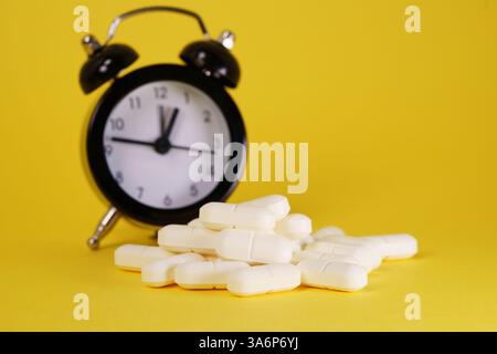 Tempo per il concetto di medicina con un orologio e un gruppo di pillole mediche sparse su sfondo giallo. Foto Stock