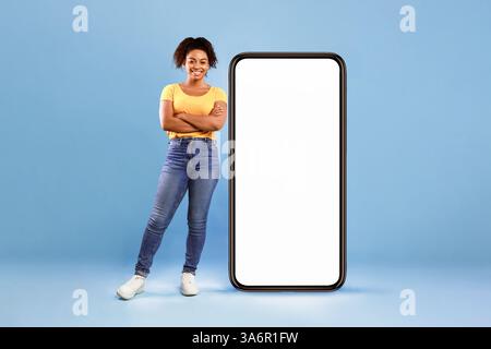 Bella signora afroamericana in piedi vicino a un enorme smartphone Foto Stock