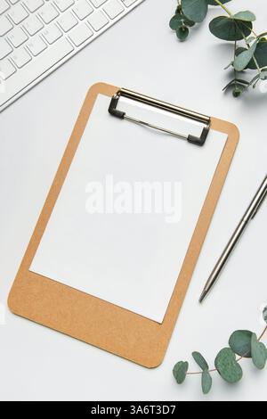 Scrivania da ufficio con appunti vuoti, tastiera, penna e rami di eucalipto su sfondo bianco Foto Stock