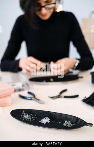 Strumenti e materiali per la creazione di gioielli su uno spazio di lavoro con un artigiano sullo sfondo. Gioielli fatti a mano, lavorazione artigianale, artigianato creativo, fai da te Foto Stock
