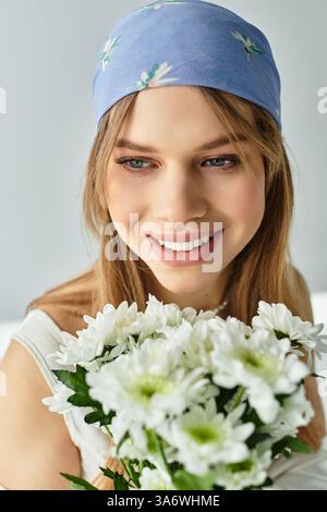 Una giovane donna alla moda tiene margherite fresche, trasudando un'allegra atmosfera primaverile in un moderno studio. Foto Stock