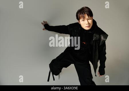 Il giovane uomo con un abbigliamento alla moda ha una posa espressiva su uno sfondo minimalista. Foto Stock