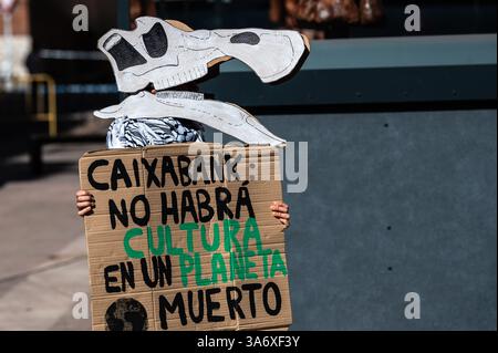 Madrid, Spagna. 26 marzo 2025. Attivista per il clima del gruppo Extinction Rebellion che indossa la maschera di dinosauro protesta di fronte alla mostra dei dinosauri della Patagonia al CaixaForum per denunciare che il gruppo CaixaBank continua ad aumentare i suoi investimenti nell'industria dei combustibili fossili. La protesta è condotta in concomitanza con la giornata mondiale del clima. Crediti: Marcos del Mazo/Alamy Live News Foto Stock