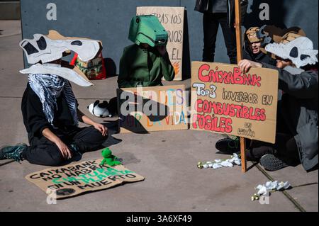 Madrid, Spagna. 26 marzo 2025. Attivisti per il clima del gruppo Extinction Rebellion che indossano maschere di dinosauri che protestano di fronte alla mostra dei dinosauri della Patagonia al CaixaForum per denunciare che il gruppo CaixaBank continua ad aumentare i suoi investimenti nell'industria dei combustibili fossili. La protesta è condotta in concomitanza con la giornata mondiale del clima. Crediti: Marcos del Mazo/Alamy Live News Foto Stock