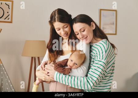 Due amate mamme adorano un momento di tenerezza con il proprio bambino in una casa accogliente per la festa della mamma. Foto Stock
