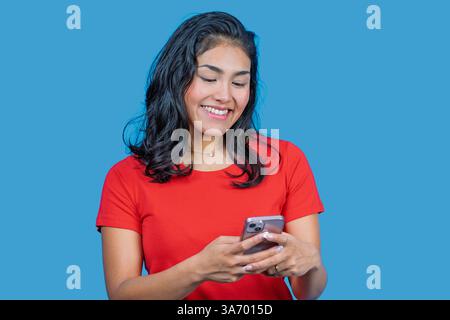 Giovane donna latina sorridente e che usa il telefono cellulare su sfondo blu Foto Stock