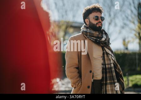 Uomo elegante con sciarpa a scacchi e occhiali da sole in piedi con sicurezza all'aperto Foto Stock