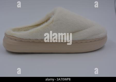 Cose da donna belle e insolite, scarpe per la casa di tutti i giorni. Pantofole bianche calde e morbide in pelliccia sintetica con suola marrone e beige spessa. Foto Stock
