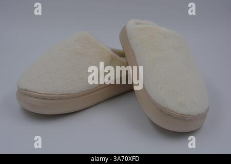 Cose da donna belle e insolite, scarpe per la casa di tutti i giorni. Pantofole bianche calde e morbide in pelliccia sintetica con suola marrone e beige spessa. Foto Stock