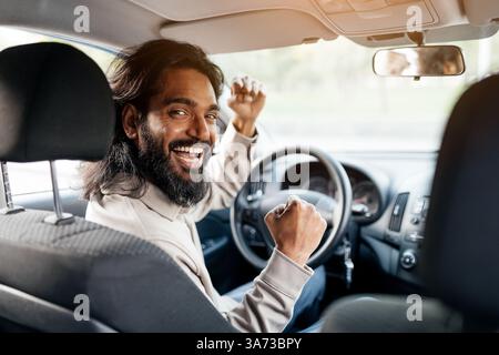 Un uomo indiano entusiasta sul sedile del conducente che festeggia con gioia con i pugni rialzati Foto Stock