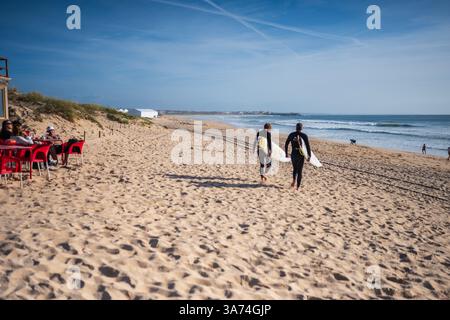 Due surfisti che camminano nelle acque della spiaggia di Supertubos, Peniche Foto Stock