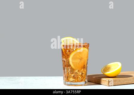Cocktail con tè di ghiaccio a Long Island e rum. Bicchiere di tè ghiacciato con fette di limone e ghiaccio schiantato su sfondo grigio neutro alla moda, copia spazio. Homemad Foto Stock