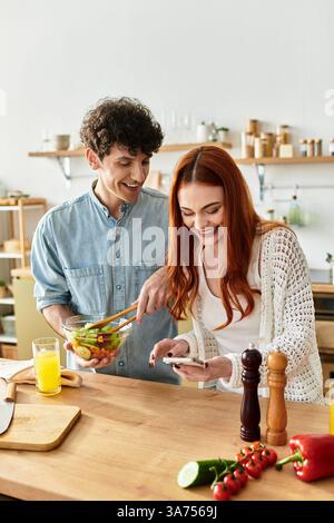 Una giovane coppia condivide momenti di gioia mentre prepara un'insalata fresca insieme. Foto Stock