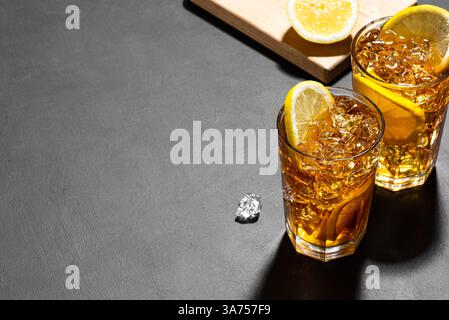 Cocktail con tè di ghiaccio a Long Island e rum. Due bicchieri di tè freddo con fette di limone e ghiaccio schiantato su sfondo di ardesia nera, copia spazio. Fatti in casa Foto Stock