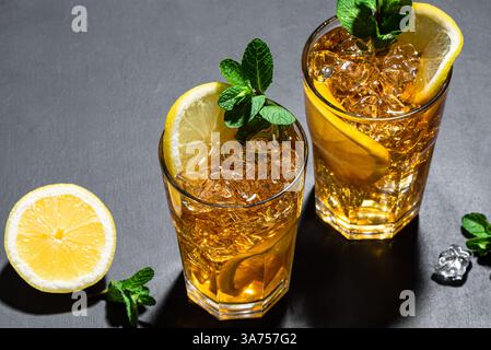 Cocktail con tè di ghiaccio a Long Island. Due bicchieri di tè freddo con fette di limone, menta e ghiaccio su sfondo nero. Bevanda fredda estiva fatta in casa. Foto Stock