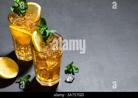 Cocktail con tè di ghiaccio a Long Island. Due bicchieri di tè freddo con fette di limone, menta e ghiaccio su sfondo nero, luce rigida alla moda, spazio per copie. Homem Foto Stock