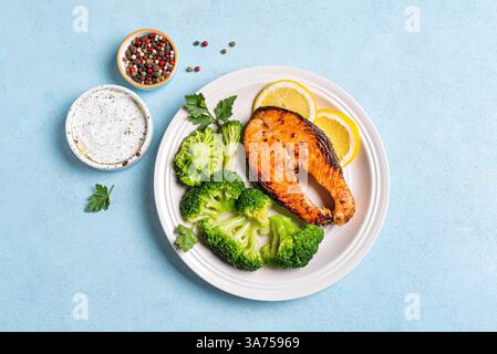 Bistecca di pesce al salmone arrosto con broccoli al vapore e salsa di yogurt su sfondo blu, vista dall'alto. Concetto di cibo sano ed equilibrato, chetogeno muore Foto Stock