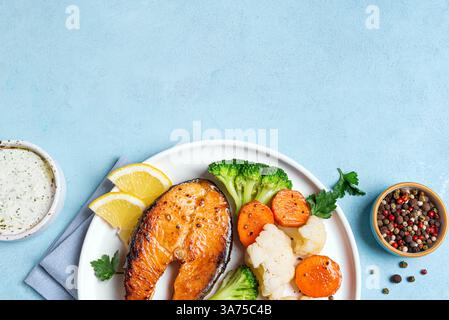Bistecca di pesce al salmone arrosto con verdure al vapore e salsa di yogurt su sfondo blu, vista dall'alto, spazio copia. Cibo mediterraneo sano ed equilibrato Foto Stock