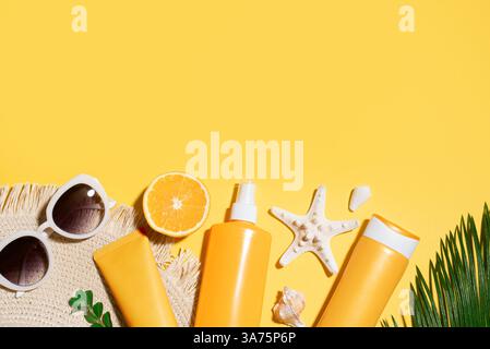 Vacanze estive, protezione UV. Prodotti per crema solare arancione, occhiali da sole, cappello di paglia su sfondo giallo, spazio copia, banner. Protezione solare SPF cosmet Foto Stock