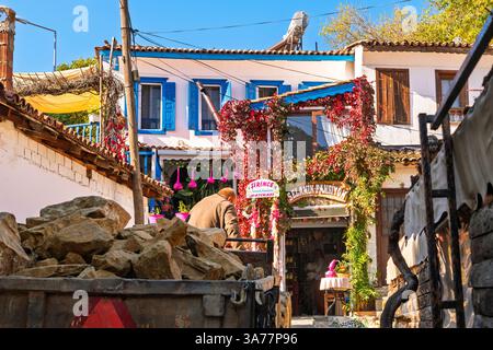 Un piccolo camion per lavori di costruzione che trasporta massi guida lungo un vicolo acciottolato nel vivace centro storico di Sirince, in Turchia. Foto Stock