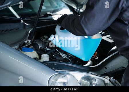 Uomo che versa il lavavetri dal contenitore in plastica nel serbatoio dell'auto, primo piano Foto Stock