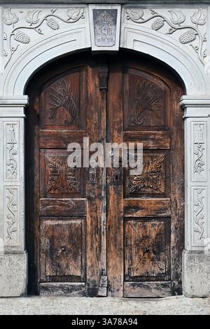 Porta ornata in legno antico con motivi intagliati, incastonata in una cornice decorativa in pietra nel villaggio di Stara Fužina, vicino al lago di Bohinj, alle Alpi Giulie, in Slovenia Foto Stock
