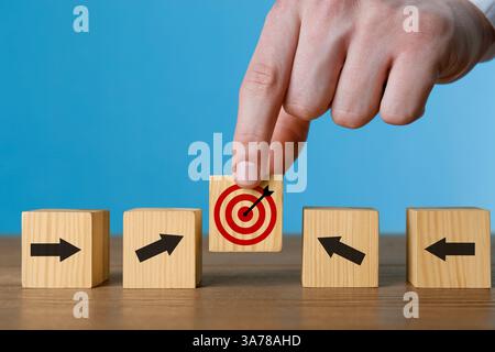 Targeting. Uomo che mette il cubo con il bullseye tra gli altri con frecce sul tavolo di legno, primo piano Foto Stock