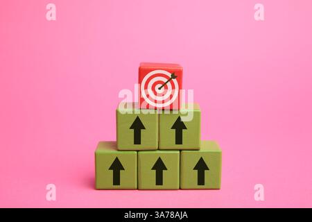 Targeting. Piramide di cubi con frecce che puntano verso una rossa con un mirino sulla parte superiore su sfondo rosa Foto Stock