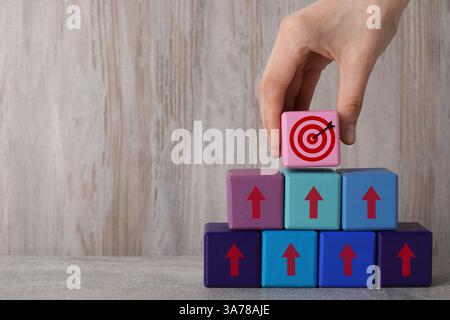Targeting. Donna che mette il cubo con il busto sulla piramide di altre con frecce sul tavolo di legno, primo piano Foto Stock