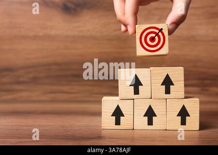 Targeting. Donna che mette il cubo con il busto sulla piramide di altre con frecce sul tavolo di legno, primo piano Foto Stock