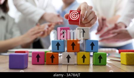 Targeting. Donna che mette il cubo con il busto sulla piramide di altre con frecce sul tavolo di legno, primo piano Foto Stock