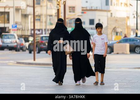 Jeddah, Arabia Saudita - 08 marzo 2023, due donne arabe vestite di paranja, burqa e ragazzo arabo che attraversano la strada, di giorno, nella città vecchia di Jeddah, Foto Stock