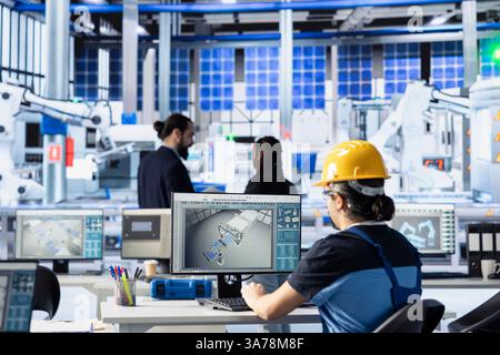 Ingegnere in fabbrica di tecnologia solare che esamina i registri di sistema sul computer per identificare le inefficienze operative. I dipendenti dell'impianto fotovoltaico monitorano i dati sul PC, regolando i parametri di produzione Foto Stock