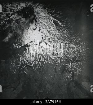 Una drammatica immagine topografica aerea dell'Etna, l'iconico stratovulcano siciliano, catturato da un aereo da ricognizione militare statunitense nell'Italia del dopoguerra. Scattata alla fine degli anni '1940, la fotografia rivela flussi lavici ricoperti di neve e fessure radiali che scendono dal cratere sommitale. Questa immagine è stata utilizzata in indagini geologiche per valutare l'attività vulcanica e il terreno sulla scia della seconda guerra mondiale Foto Stock