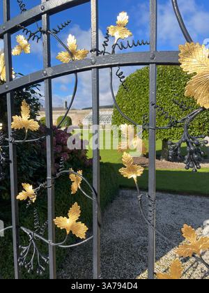 Cancello artistico in ferro battuto con dettagli in foglia d'oro in un giardino irlandese in una giornata di sole. Foto Stock