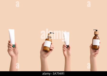 Mani femminili con provette e bottiglie diversi prodotti cosmetici su sfondo beige Foto Stock