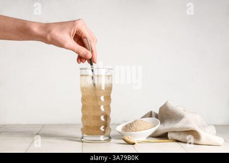 Mano femminile con cucchiaio e buccia di psico in un bicchiere d'acqua sul tavolo Foto Stock