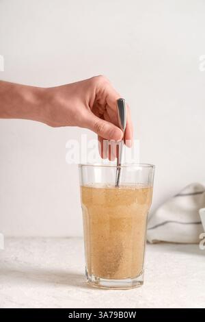 Mano femminile con cucchiaio e buccia di psico in un bicchiere d'acqua su sfondo chiaro Foto Stock