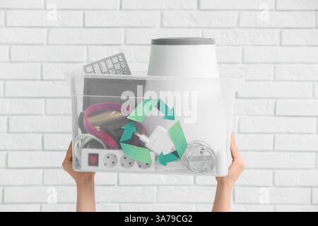 Mani femminili con rifiuti elettronici per il riciclaggio in contenitori su sfondo bianco in mattoni Foto Stock