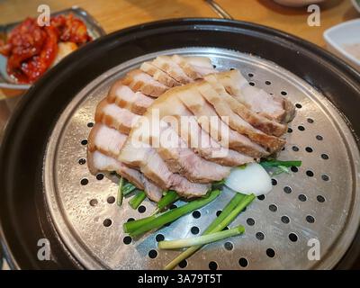 Soffice bossam coreano a fette (pancetta di maiale bollita) servito su un vassoio per la cottura a vapore Completato da un lato di kimchi piccante. Una classica prelibatezza coreana. Foto Stock