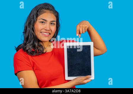 Giovane donna che punta verso un tablet digitale con schermo vuoto su sfondo blu Foto Stock